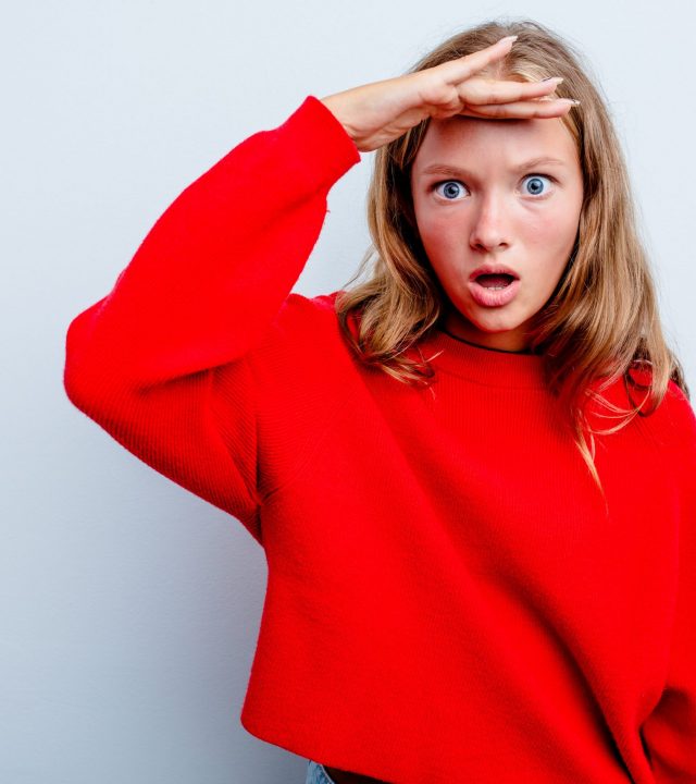 Caucasian teen girl isolated on blue background looking far away keeping hand on forehead.